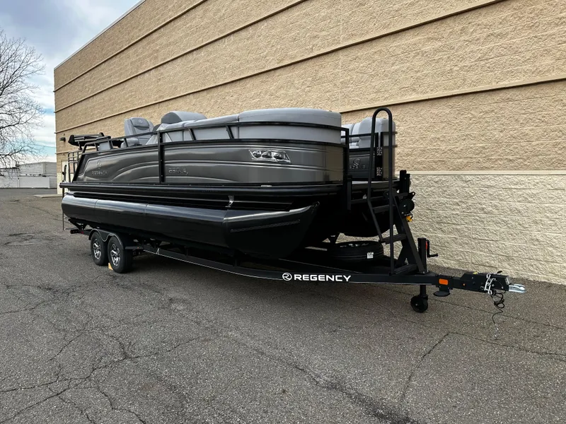 Slide: The Image of 2024 Regency 230 LE3 Sport pontoon boat on trailer, parked beside a beige building. - 9