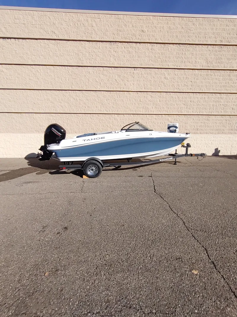 Slide: The Image of 2024 Tahoe 200 S boat on trailer, parked outdoors against a beige wall. - 2