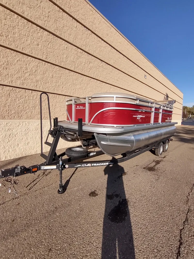 Slide: The Image of 2024 Sun Tracker Party Barge 20 DLX pontoon boat on trailer, parked by a beige wall. - 3
