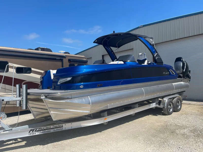 The Image of 2024 Manitou 25 XT SHP DE pontoon boat on trailer, blue exterior. - 1