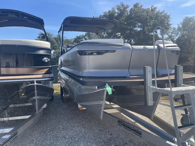 Slide: The Image of 2024 Manitou Explore 26 SHP pontoon boat on a trailer, displayed outdoors. - 7