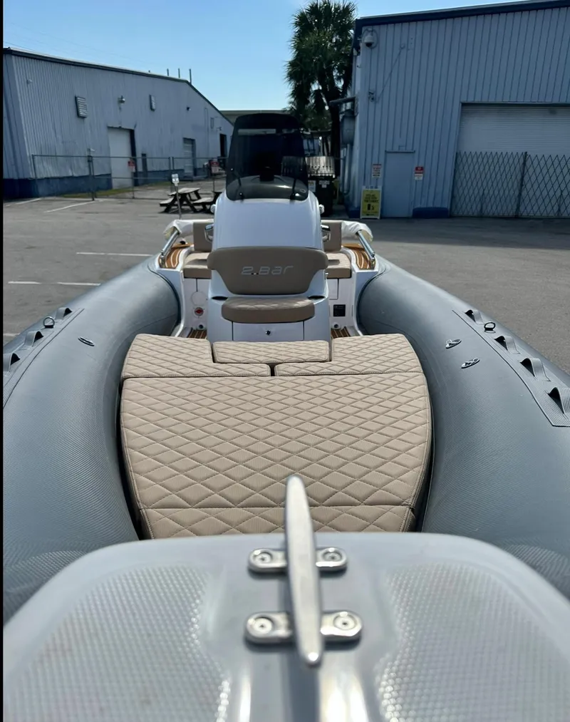 Slide: The Image of 2023 2 Bar 6.20 inflatable boat with beige quilted seating, docked at a marina. - 12