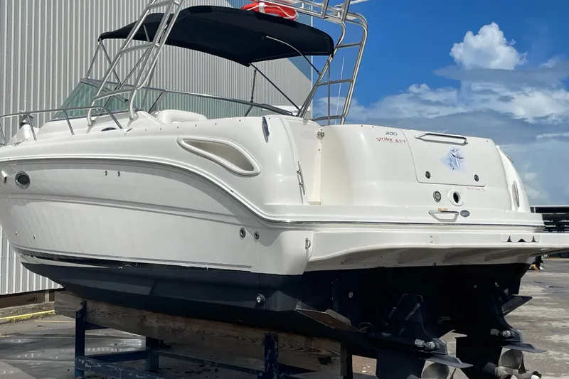 Slide: The Image of 2006 Sea Ray 290 Amberjack boat on dry dock, white hull, blue canopy, clear sky background. - 46