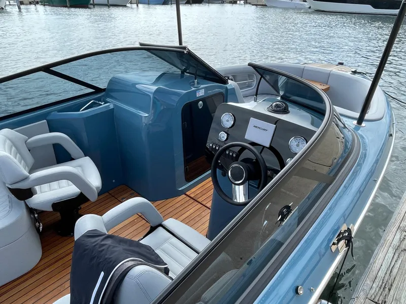 Slide: The Image of 2022 Cranchi 26 Rider boat interior with modern dashboard and seating, docked by the water. - 13