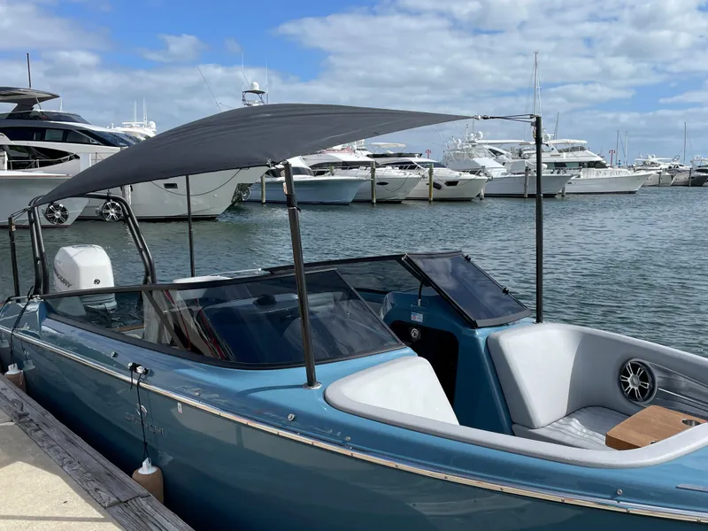 Slide: The Image of 2022 Cranchi 26 Rider boat docked at marina with canopy, surrounded by yachts. - 2