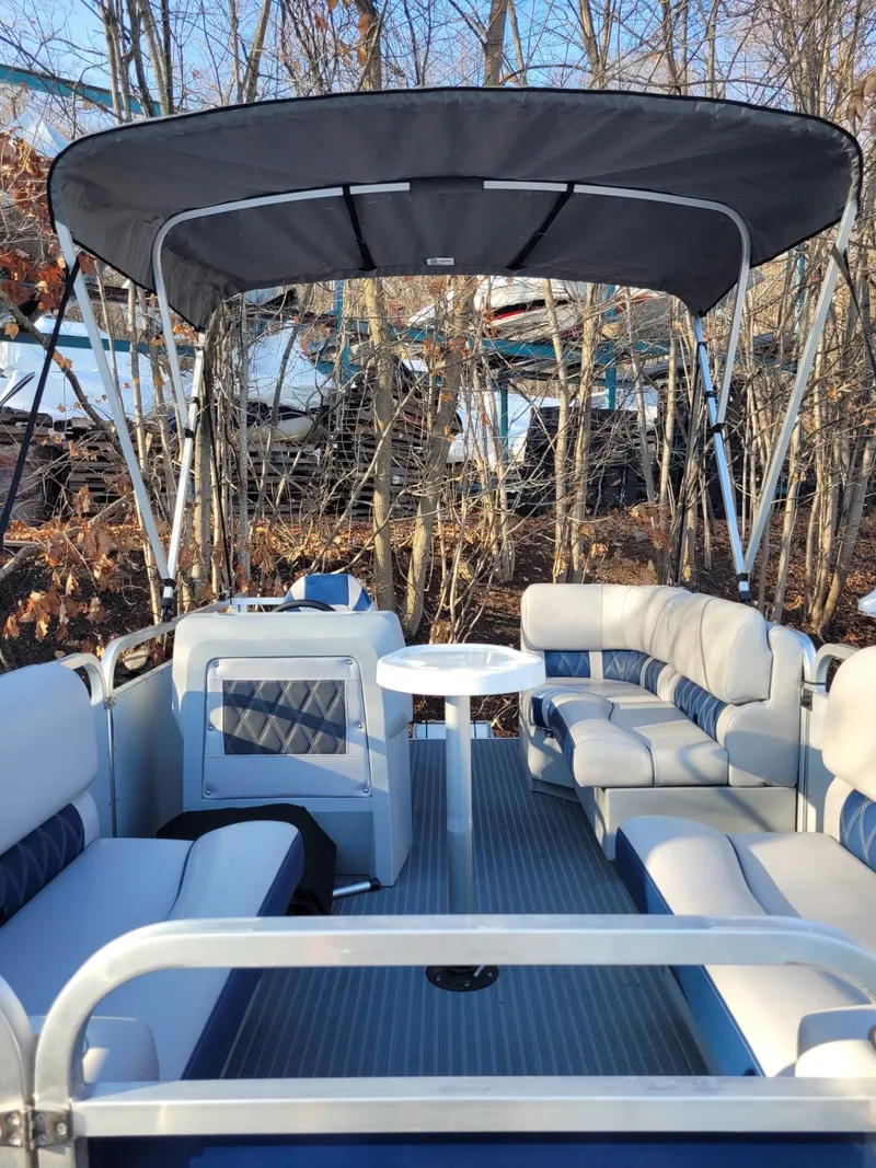 Slide: The Image of 2024 Pond-Tini Series 14 pontoon boat with canopy and seating, docked near trees. - 2