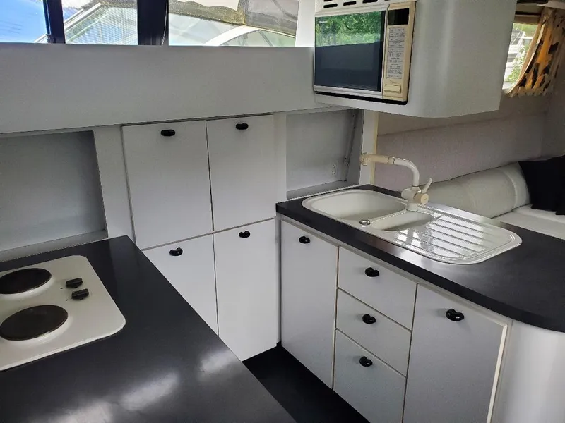 Slide: The Image of 1990 Mainship Mediterranean yacht kitchen with stove, sink, microwave, and white cabinetry. - 12
