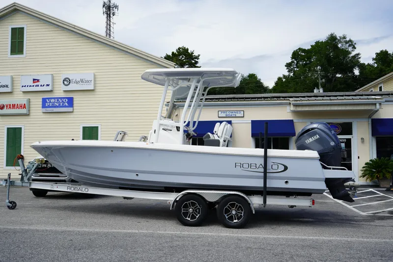 Slide: The Image of 2024 Robalo 226 Cayman boat on trailer, parked outside dealership with signage. - 0