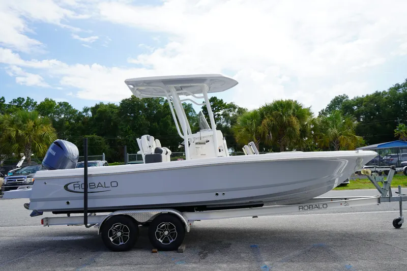 Slide: The Image of 2024 Robalo 226 Cayman boat on trailer, parked outdoors with trees in background. - 2