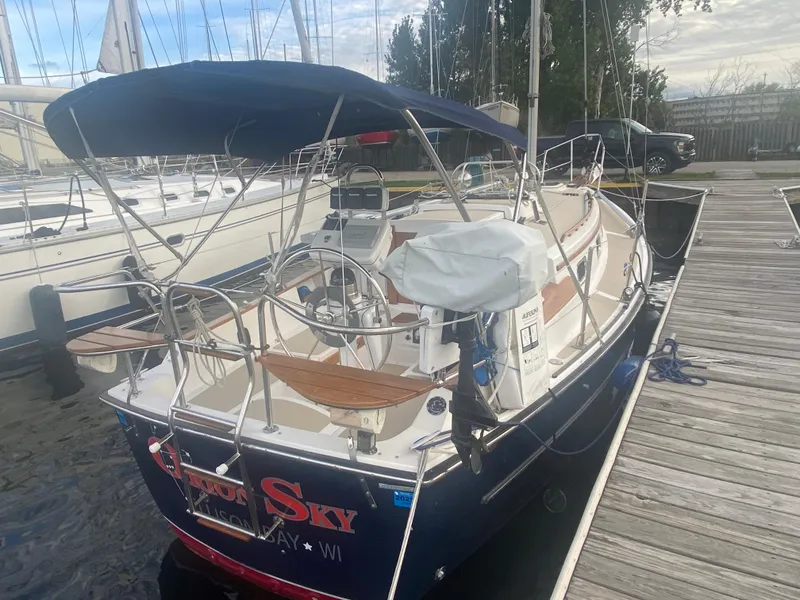 Slide: The Image of 2014 Com-Pac 27 sailboat docked at marina with blue hull and covered cockpit. - 2