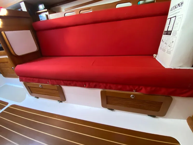 Slide: The Image of Interior of 2014 Com-Pac 27 sailboat with red cushioned seating and wooden storage compartments. - 21