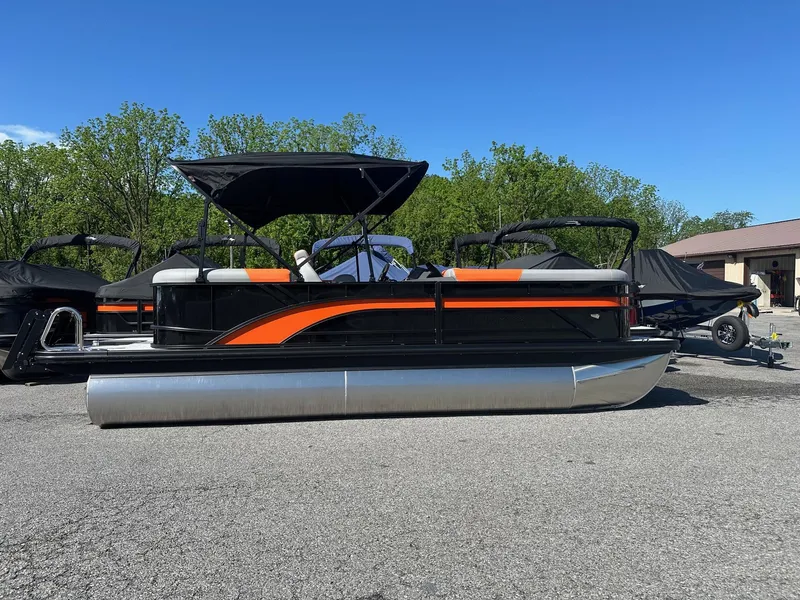 Slide: The Image of 2025 Bennington 21 SSR Quad Bench pontoon boat with black and orange design, parked outdoors. - 22