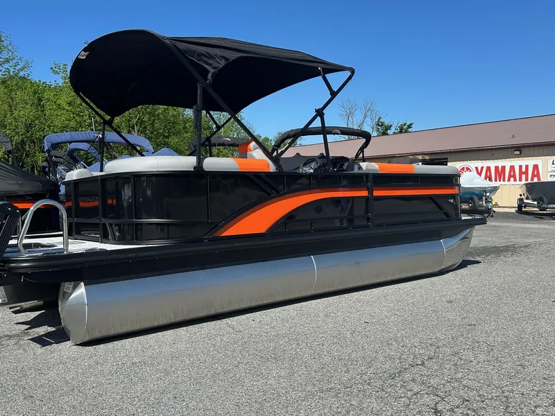 Slide: The Image of 2025 Bennington 21 SSR Quad Bench pontoon boat with black and orange design, parked outdoors. - 3