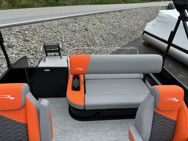 Slide: The Image of 2025 Bennington 22 SSB Swing Back boat with orange and gray seating, docked near a road. - 14