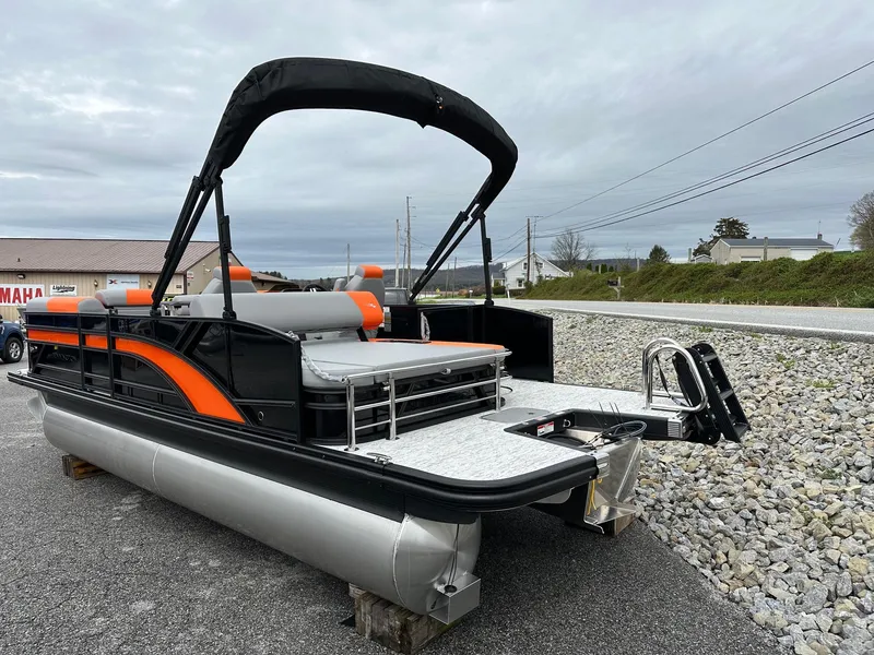 Slide: The Image of 2025 Bennington 22 SSB Swing Back pontoon boat with orange accents, parked on gravel. - 18