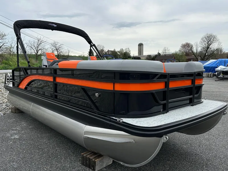 Slide: The Image of 2025 Bennington 22 SSB Swing Back pontoon boat with orange and black accents, parked outdoors. - 19