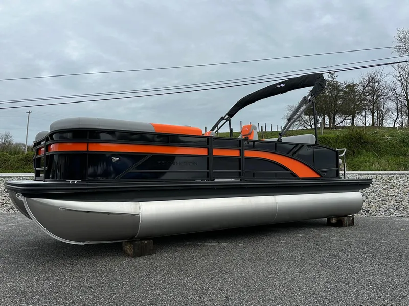 Slide: The Image of 2025 Bennington 22 SSB Swing Back pontoon boat with orange and black design, parked on gravel. - 4