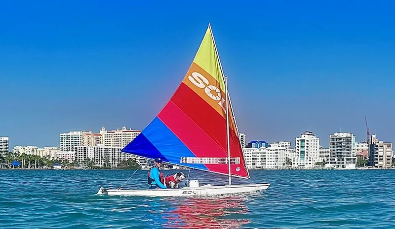 Slide: The Image of 2024 Dinghy Sol Sailboat on water with colorful sail, city skyline in background. - 15