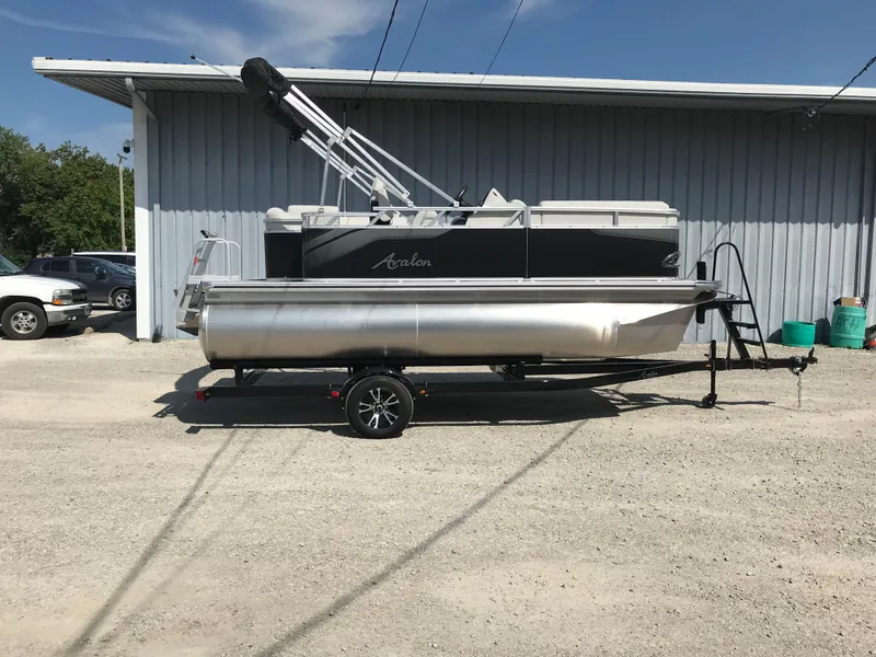 Slide: The Image of 2024 Avalon VTX Cruise pontoon boat on trailer, parked outside a garage. - 1