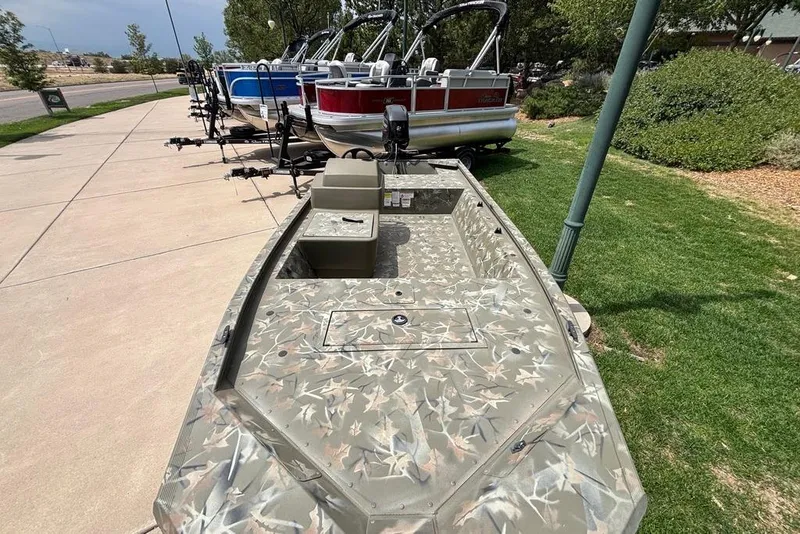 Slide: The Image of 2024 Tracker Grizzly 1648 SC boat with camouflage design, displayed outdoors on a sunny day. - 2