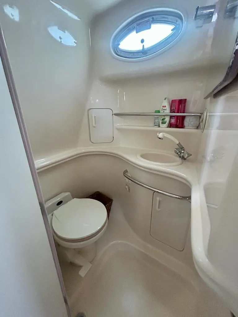 Slide: The Image of 2002 Sea Ray 340 Sundancer bathroom with compact design, oval window, and storage shelves. - 4