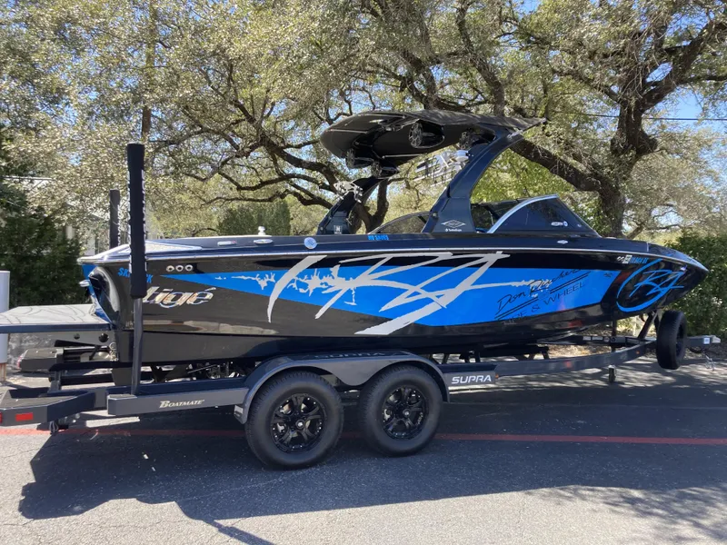 The Image of 2011 Tigé RZ2 boat on a trailer with custom blue and black graphics. - 1