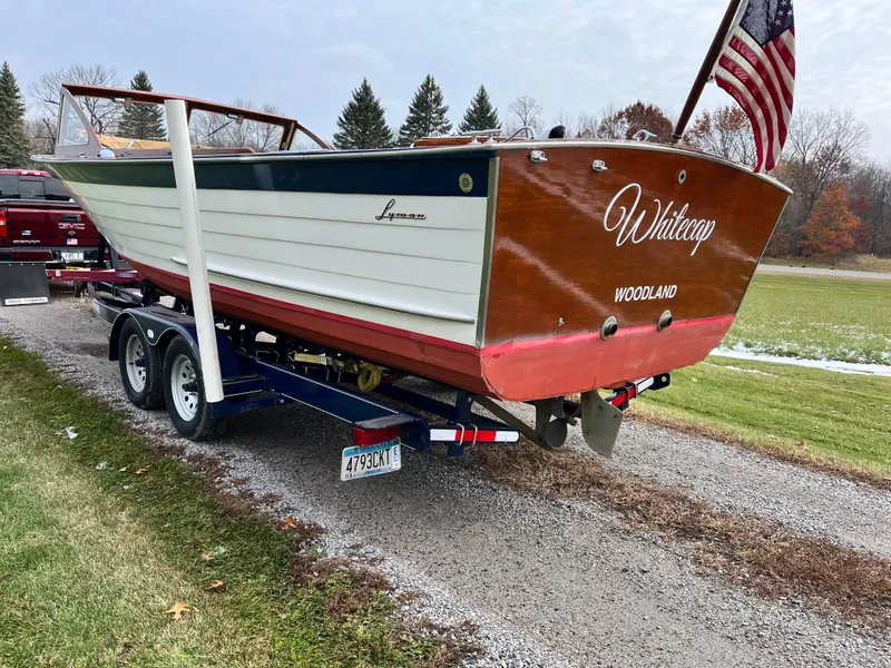 Slide: The Image of 1963 Lyman Sportsman boat on trailer, named "Whitecap," with American flag, parked on gravel path. - 3