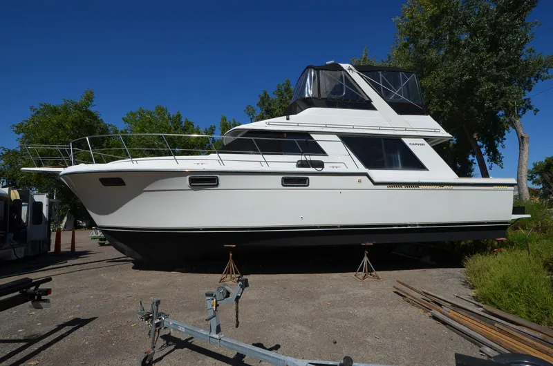 Slide: The Image of 1986 Carver Cockpit 4227 MY yacht on land, surrounded by trees and clear sky. - 2