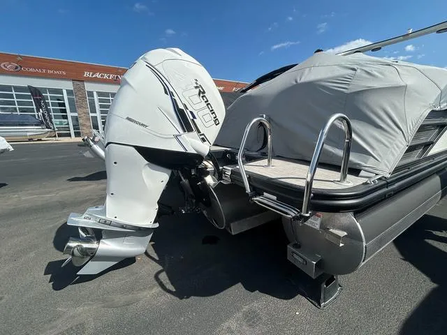Slide: The Image of 2023 Bennington 25 RFBWA Tritoon with powerful outboard motor, covered and parked outdoors. - 25