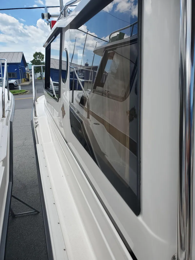 Slide: The Image of 2020 Ranger Tugs 25 boat side view with reflective windows and clear sky. - 23