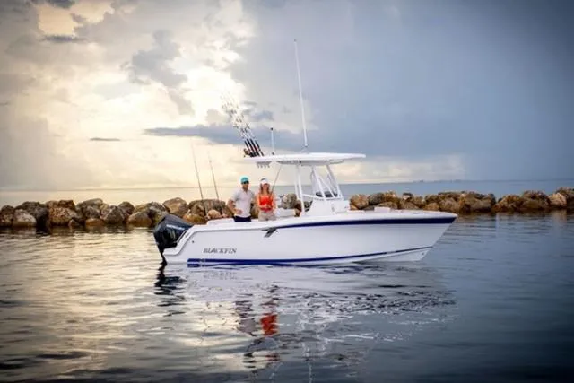 Slide: The Image of 2024 Blackfin 222CC boat on calm water near rocky shoreline under cloudy sky. - 10