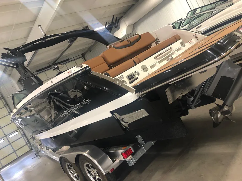 Slide: The Image of 2024 Chaparral 28 Surf boat in showroom, featuring sleek design and dual-axle trailer. - 2
