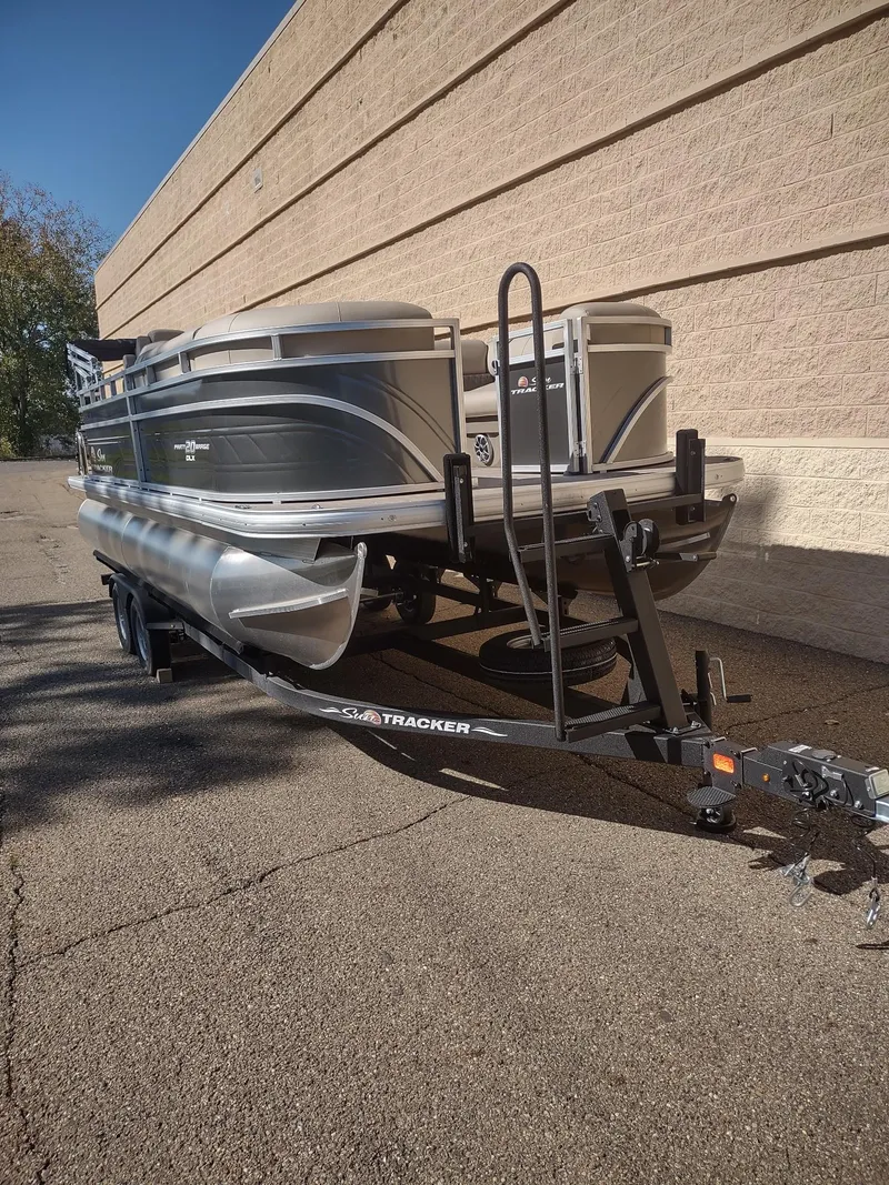 Slide: The Image of 2024 Sun Tracker Party Barge 20 DLX pontoon boat on trailer, parked outdoors. - 2