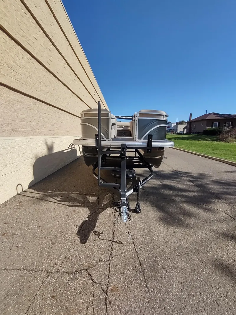 Slide: The Image of 2024 Sun Tracker Party Barge 20 DLX on trailer, parked beside a building. - 3