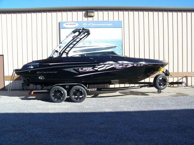 The Image of 2024 Crownline 240LPX black boat on trailer outside a building. - 1