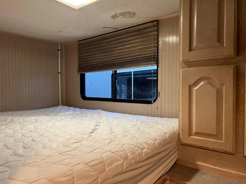 Slide: The Image of Interior of 1998 Custom Escalante share #8 RV with bed, window, and wooden cabinets. - 9