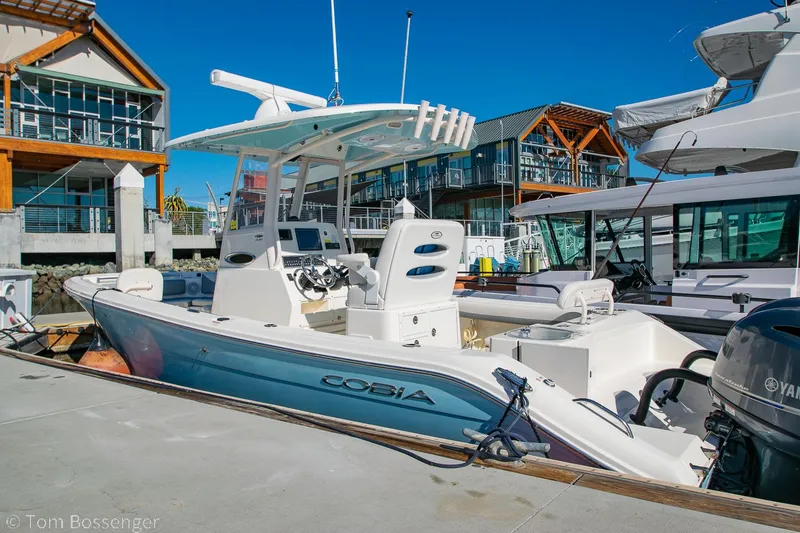 Slide: The Image of 2018 Cobia 240 CC boat docked at a marina with modern buildings in the background. - 2