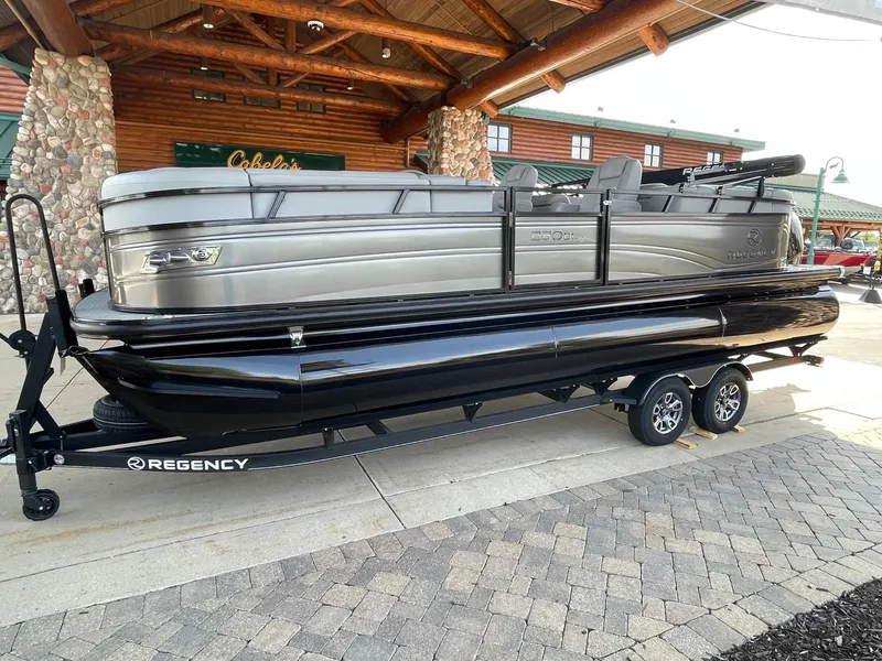 Slide: The Image of 2024 Regency 230 DL3 pontoon boat on trailer, displayed outdoors. - 1
