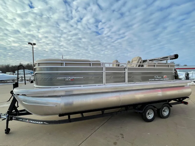 The Image of 2024 Sun Tracker Party Barge 22 XP3 pontoon boat on trailer under cloudy sky. - 0