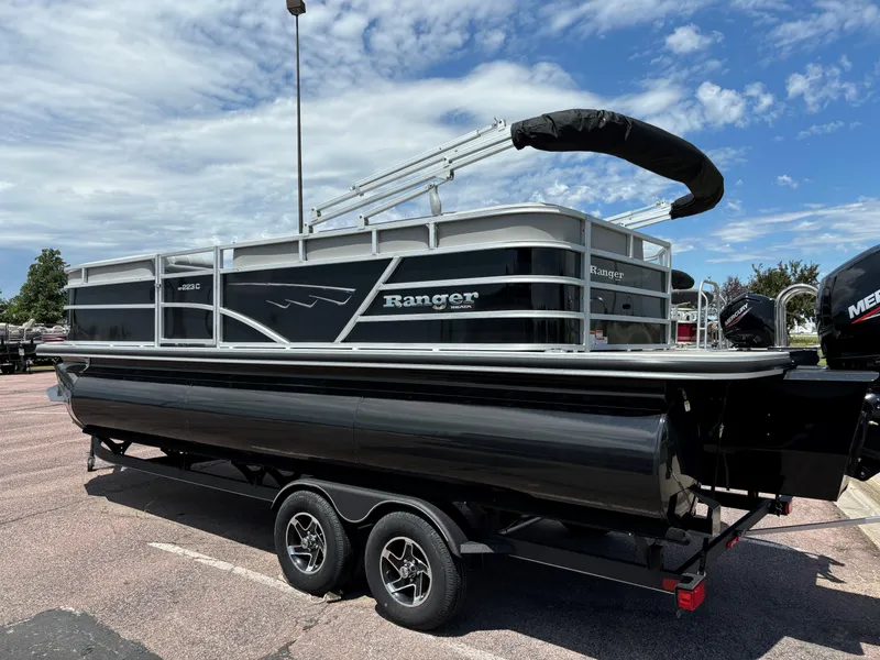 The Image of 2024 Ranger Reata 223C pontoon boat on a trailer under a blue sky. - 0