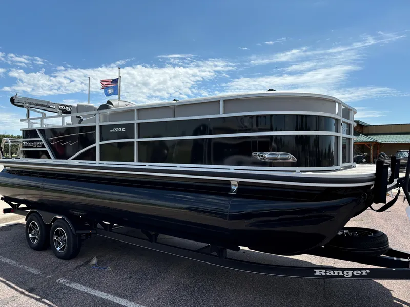 Slide: The Image of 2024 Ranger Reata 223C pontoon boat on a trailer under a clear blue sky. - 1