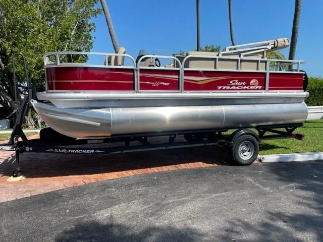 The Image of 2024 Sun Tracker Bass Buggy 18 DLX pontoon boat on a trailer, parked outdoors. - 0