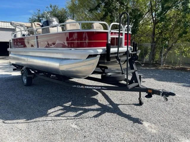 Slide: The Image of 2024 Sun Tracker Bass Buggy 18 DLX pontoon boat on a trailer in a gravel lot. - 7