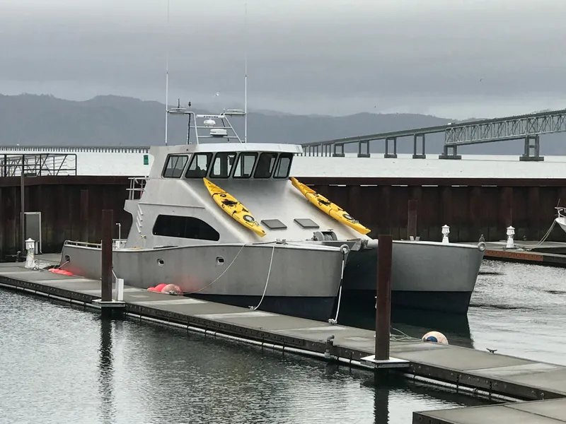 Slide: The Image of Custom 62 Catamaran (2008) docked with kayaks on deck, overcast sky, and bridge in background. - 0