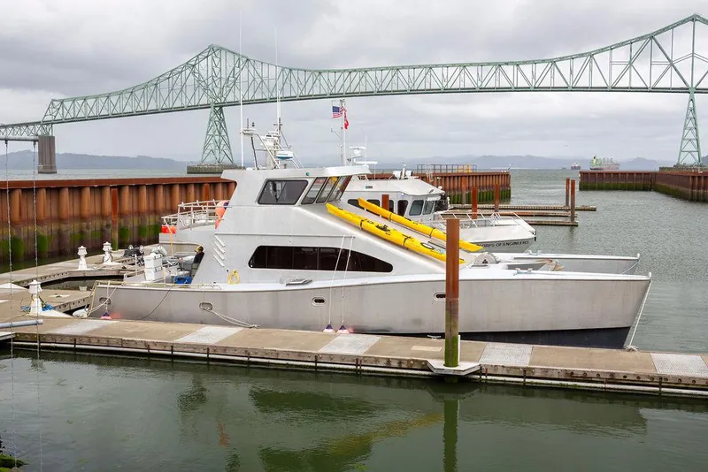 Slide: The Image of Custom 62 Catamaran (2008) docked near a bridge, featuring sleek design and yellow kayaks. - 43