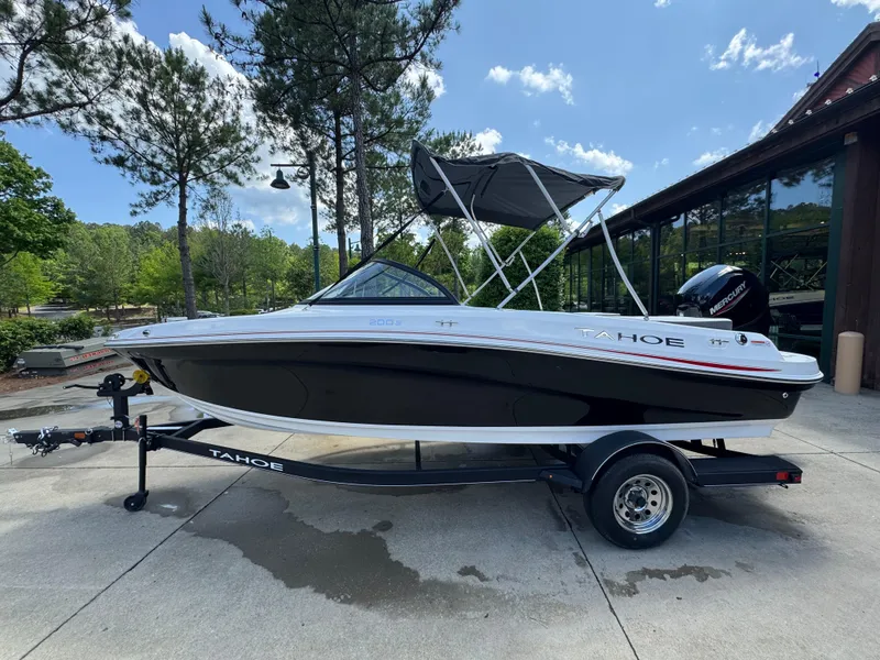 Slide: The Image of 2024 Tahoe 200 S boat on trailer, parked outdoors near trees and building. - 2