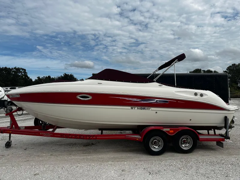 The Image of 2011 Stingray 250 LR boat on a red trailer under a cloudy sky. - 0