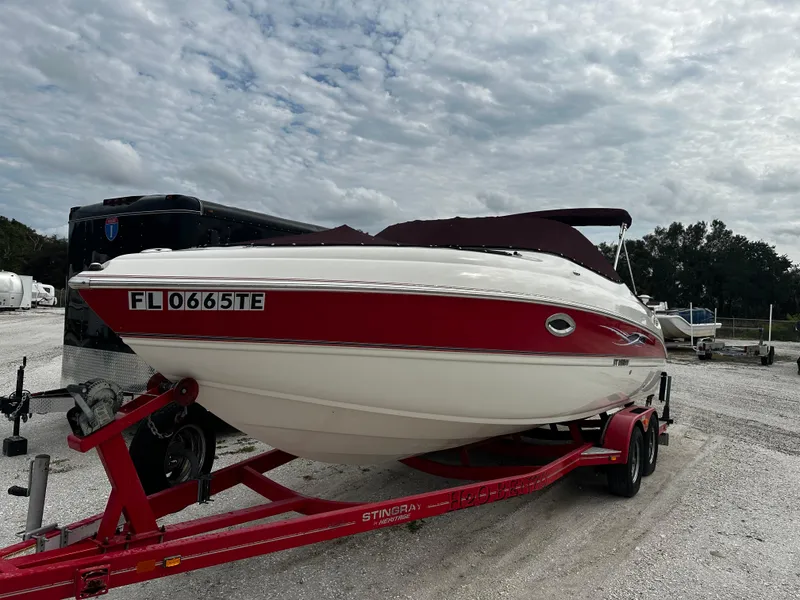 Slide: The Image of 2011 Stingray 250 LR boat on a red trailer, parked outdoors under a cloudy sky. - 1