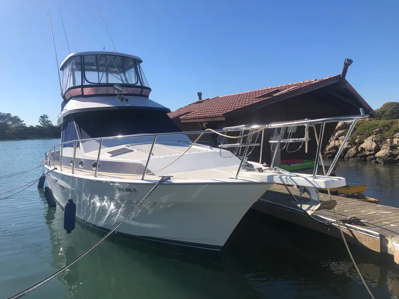The Image of 1990 Mediterranean 38 Sport Fisher boat docked by a wooden pier under clear blue skies. - 1