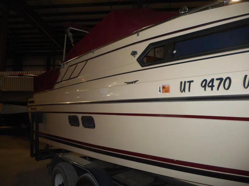Slide: The Image of 1984 Beachcraft Cabin Cruiser with maroon cover, docked indoors, side view. - 2